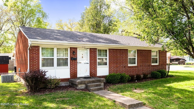 single story home with brick siding, cooling unit, a shingled roof, and a front lawn
