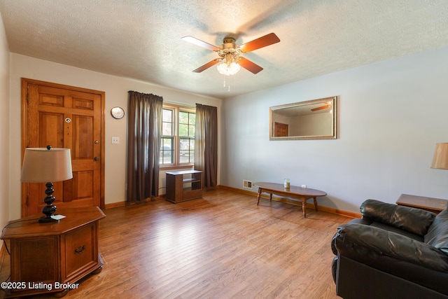 living area featuring light wood-type flooring, a textured ceiling, ceiling fan, and baseboards