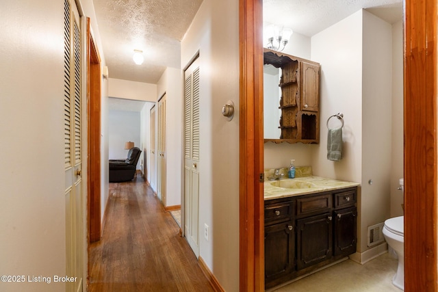 hall featuring a textured ceiling, visible vents, a sink, baseboards, and light wood-style flooring