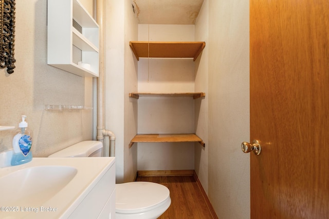 half bath with toilet, wood finished floors, and vanity