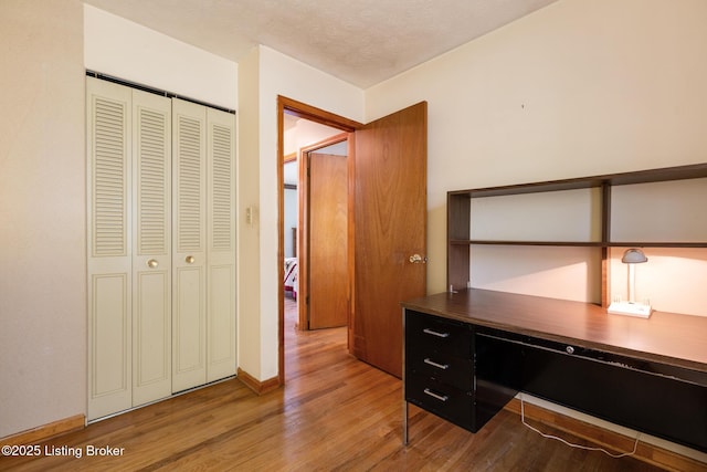 unfurnished office featuring baseboards, built in desk, and wood finished floors