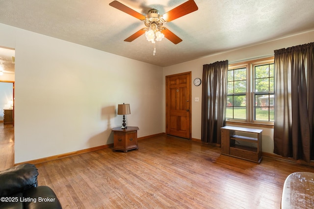 interior space with light wood-style floors, a ceiling fan, baseboards, and a textured ceiling