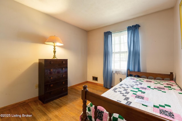 bedroom with baseboards, visible vents, and wood finished floors