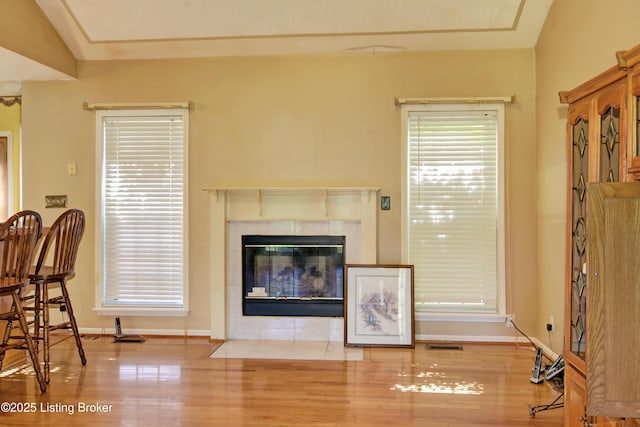 living area featuring a tiled fireplace, baseboards, wood finished floors, and visible vents