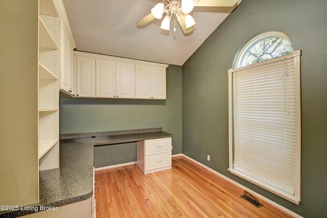unfurnished office with ceiling fan, visible vents, built in desk, lofted ceiling, and light wood-style flooring