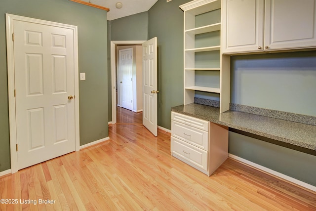 unfurnished office with baseboards, light wood finished floors, and built in desk