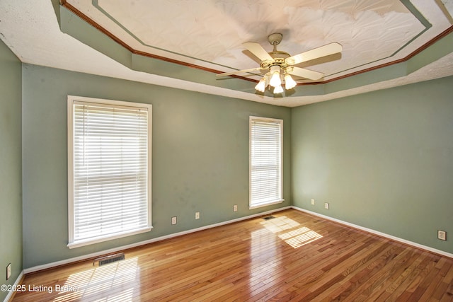 spare room featuring hardwood / wood-style flooring, visible vents, plenty of natural light, and a raised ceiling