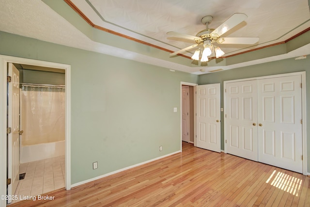 unfurnished bedroom featuring baseboards, a ceiling fan, a raised ceiling, and hardwood / wood-style flooring
