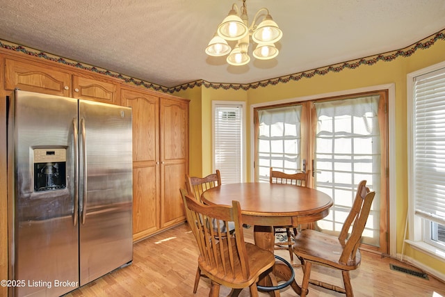 dining area with a wealth of natural light, a notable chandelier, light wood-style flooring, and visible vents