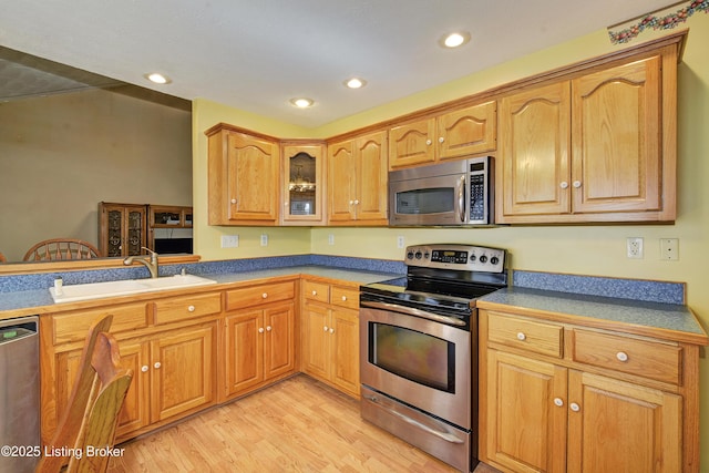 kitchen with glass insert cabinets, recessed lighting, a sink, light wood finished floors, and stainless steel appliances