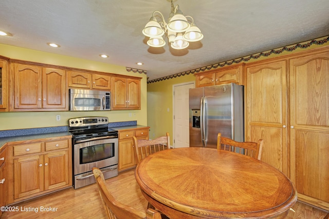 kitchen with stainless steel appliances, an inviting chandelier, brown cabinetry, and light wood-style floors