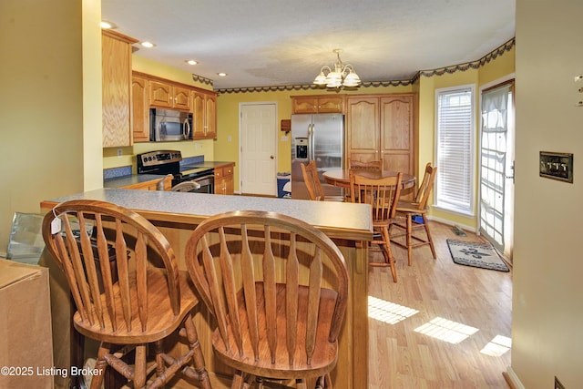 kitchen with a peninsula, light wood-type flooring, recessed lighting, appliances with stainless steel finishes, and a notable chandelier