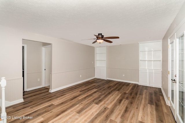 empty room featuring a textured ceiling, built in features, ceiling fan, and wood finished floors
