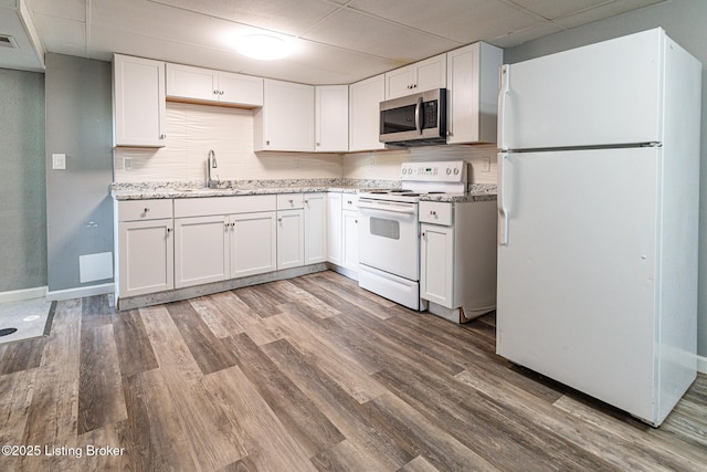 kitchen with a sink, white appliances, white cabinetry, a drop ceiling, and wood finished floors