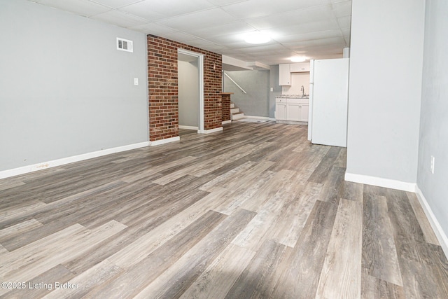 finished basement featuring visible vents, freestanding refrigerator, stairs, wood finished floors, and baseboards
