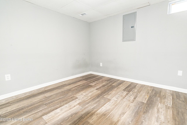 empty room featuring baseboards, electric panel, wood finished floors, and a paneled ceiling