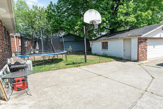 view of patio featuring a garage, a trampoline, an outbuilding, and driveway