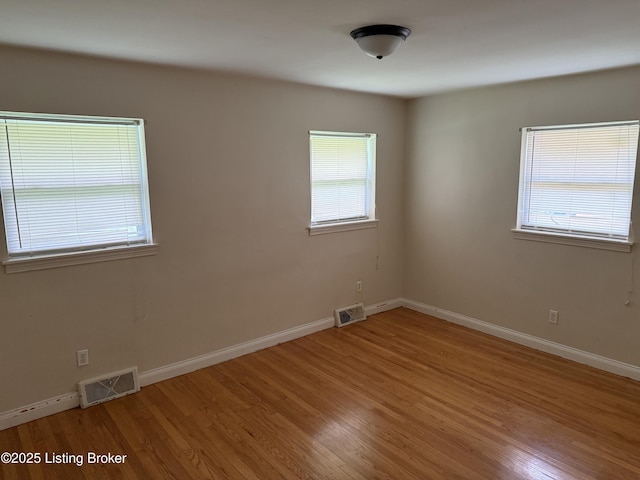 empty room featuring plenty of natural light, visible vents, and wood finished floors