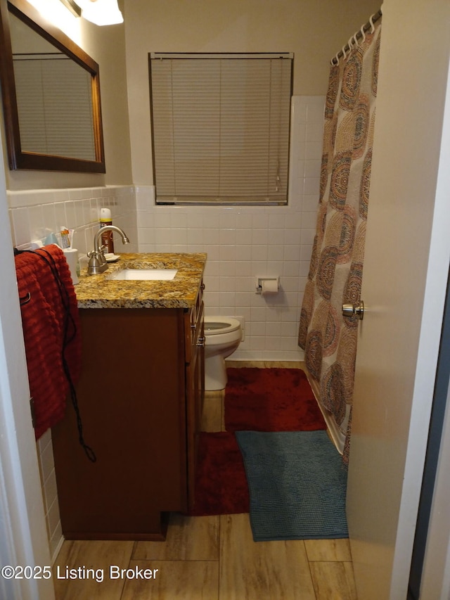 bathroom with toilet, tile walls, vanity, and wood finished floors