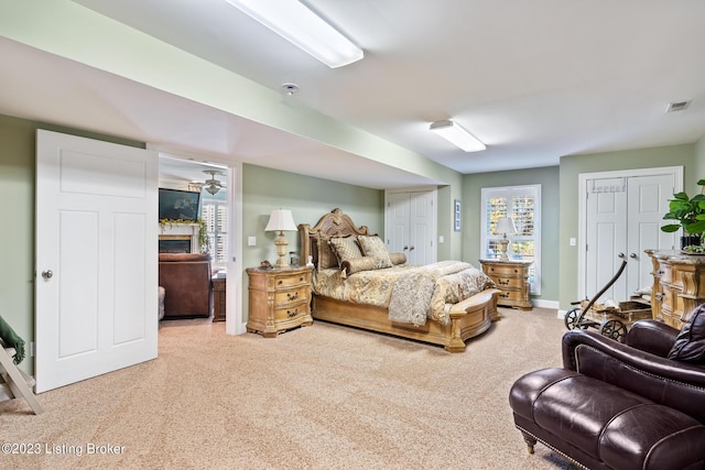 bedroom with visible vents, multiple closets, light carpet, baseboards, and a lit fireplace