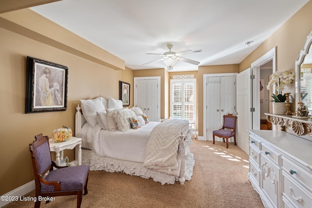 bedroom with ceiling fan, multiple closets, light carpet, and baseboards