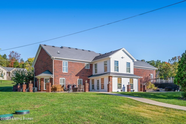 rear view of house with a yard, brick siding, and a patio