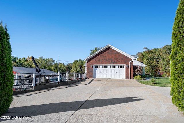 exterior space featuring concrete driveway, brick siding, fence, and a garage