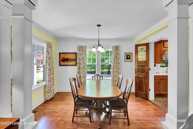 dining space featuring light wood-type flooring, a chandelier, decorative columns, and ornamental molding