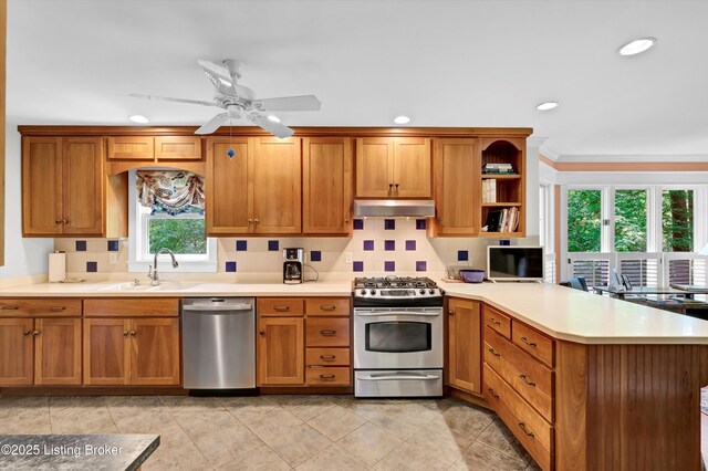 kitchen featuring a peninsula, brown cabinetry, under cabinet range hood, light countertops, and appliances with stainless steel finishes