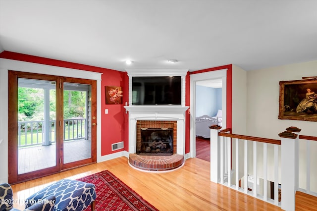 living area with baseboards, a brick fireplace, visible vents, and wood finished floors