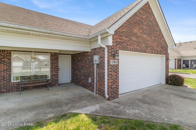 exterior space featuring brick siding, an attached garage, roof with shingles, and concrete driveway