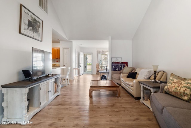 living area featuring high vaulted ceiling, light wood finished floors, and visible vents
