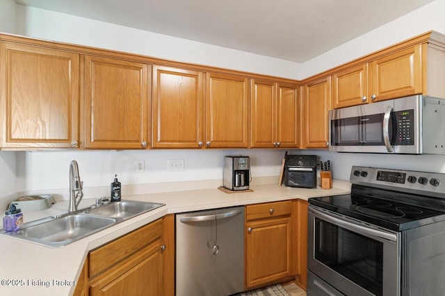 kitchen with light countertops, stainless steel appliances, brown cabinetry, and a sink