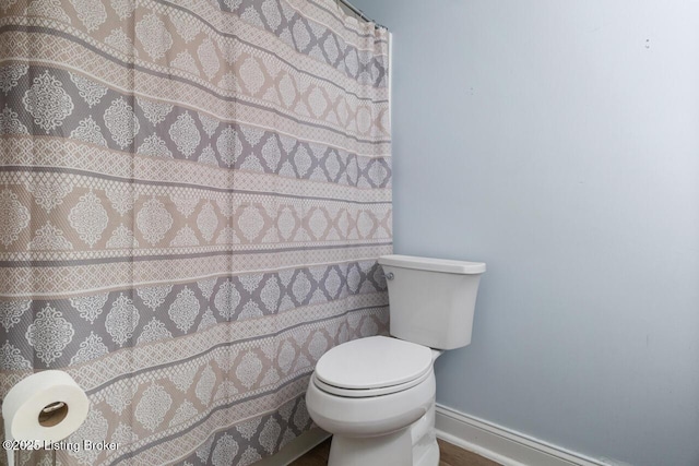 bathroom with toilet, baseboards, and a shower with curtain