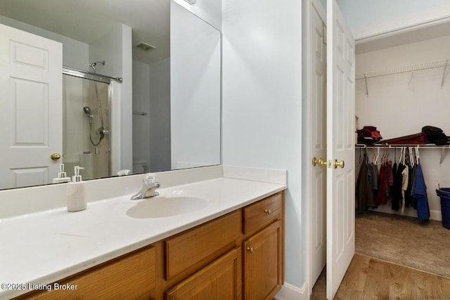 bathroom with vanity, a walk in shower, a walk in closet, and toilet