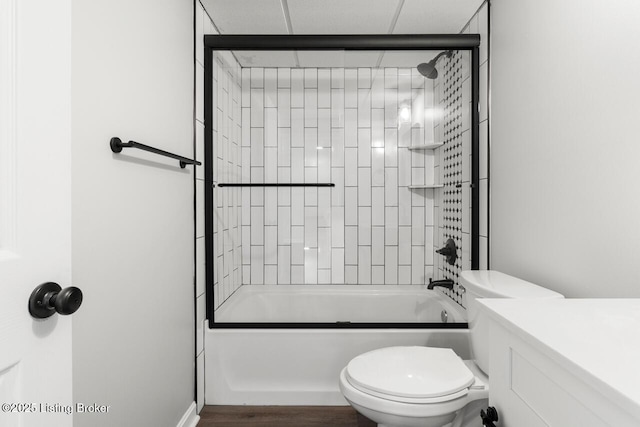 bathroom featuring toilet, bath / shower combo with glass door, vanity, and wood finished floors