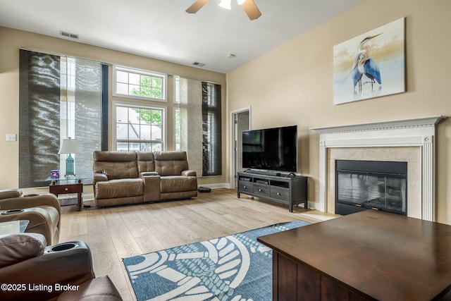 living room with a glass covered fireplace, ceiling fan, light wood finished floors, and visible vents