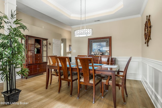 dining space with wainscoting, light wood finished floors, a tray ceiling, visible vents, and ornamental molding