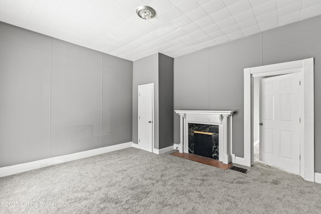 unfurnished living room with a high end fireplace, carpet flooring, and visible vents