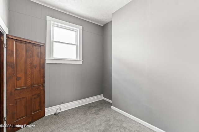 empty room featuring carpet flooring, baseboards, and crown molding
