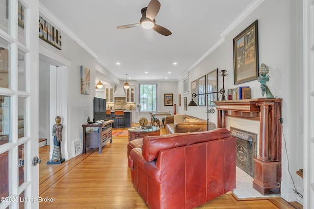 living room with a fireplace, ceiling fan, ornamental molding, light wood-type flooring, and recessed lighting