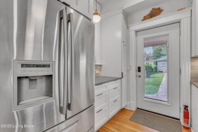 kitchen featuring stainless steel fridge with ice dispenser, white cabinets, light wood-style flooring, hanging light fixtures, and dark countertops