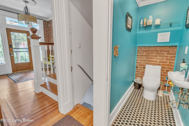 half bathroom with crown molding, toilet, baseboards, brick wall, and wood finished floors