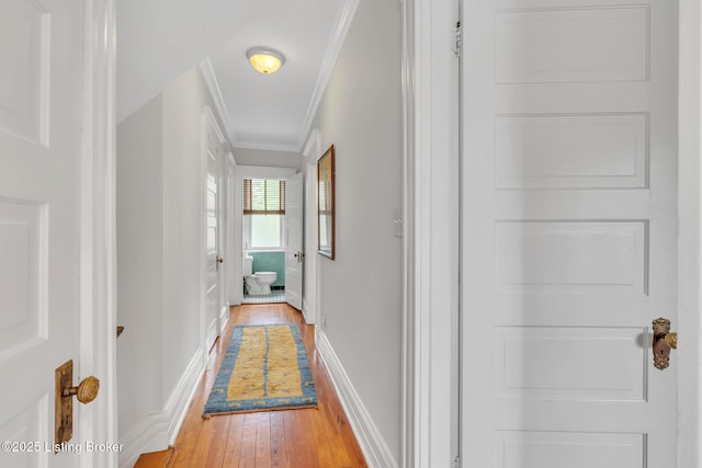 hall featuring light wood-style flooring, crown molding, and baseboards
