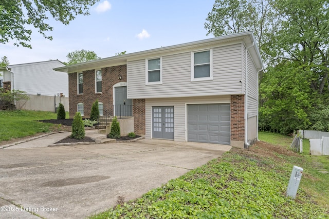 split foyer home featuring brick siding, an attached garage, driveway, and fence