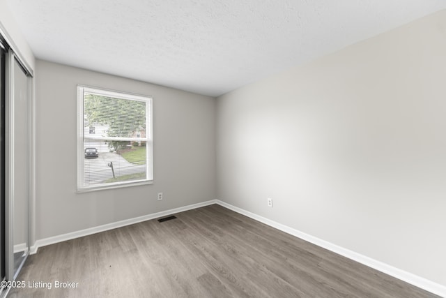 unfurnished bedroom with visible vents, a closet, wood finished floors, baseboards, and a textured ceiling