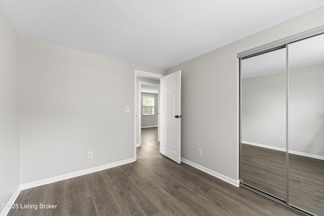 unfurnished bedroom featuring dark wood-style flooring, baseboards, and a closet