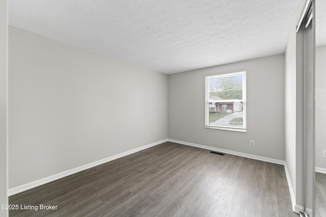 unfurnished bedroom with a textured ceiling, visible vents, dark wood-style floors, and baseboards