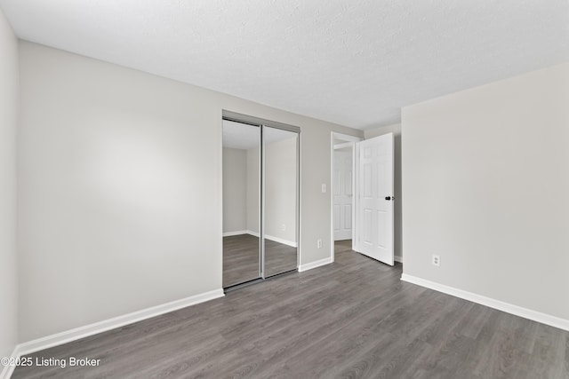 unfurnished bedroom featuring a textured ceiling, baseboards, wood finished floors, and a closet