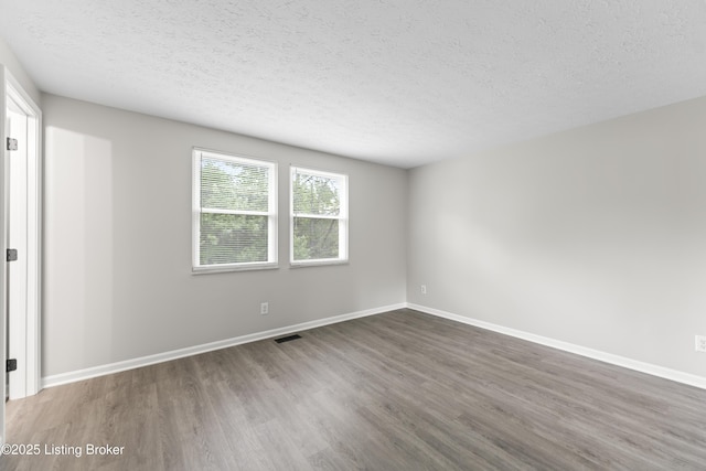 unfurnished room with dark wood-style flooring, a textured ceiling, visible vents, and baseboards